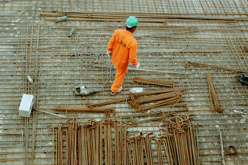 A construction worker in a green hard hat and orange jumpsuit on the worksite.